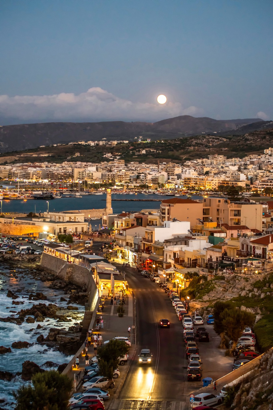 "Panoramic night view of Rethymno town from the Fortezza, featuring the Venetian harbor and the lighthouse under the light of the full moon."