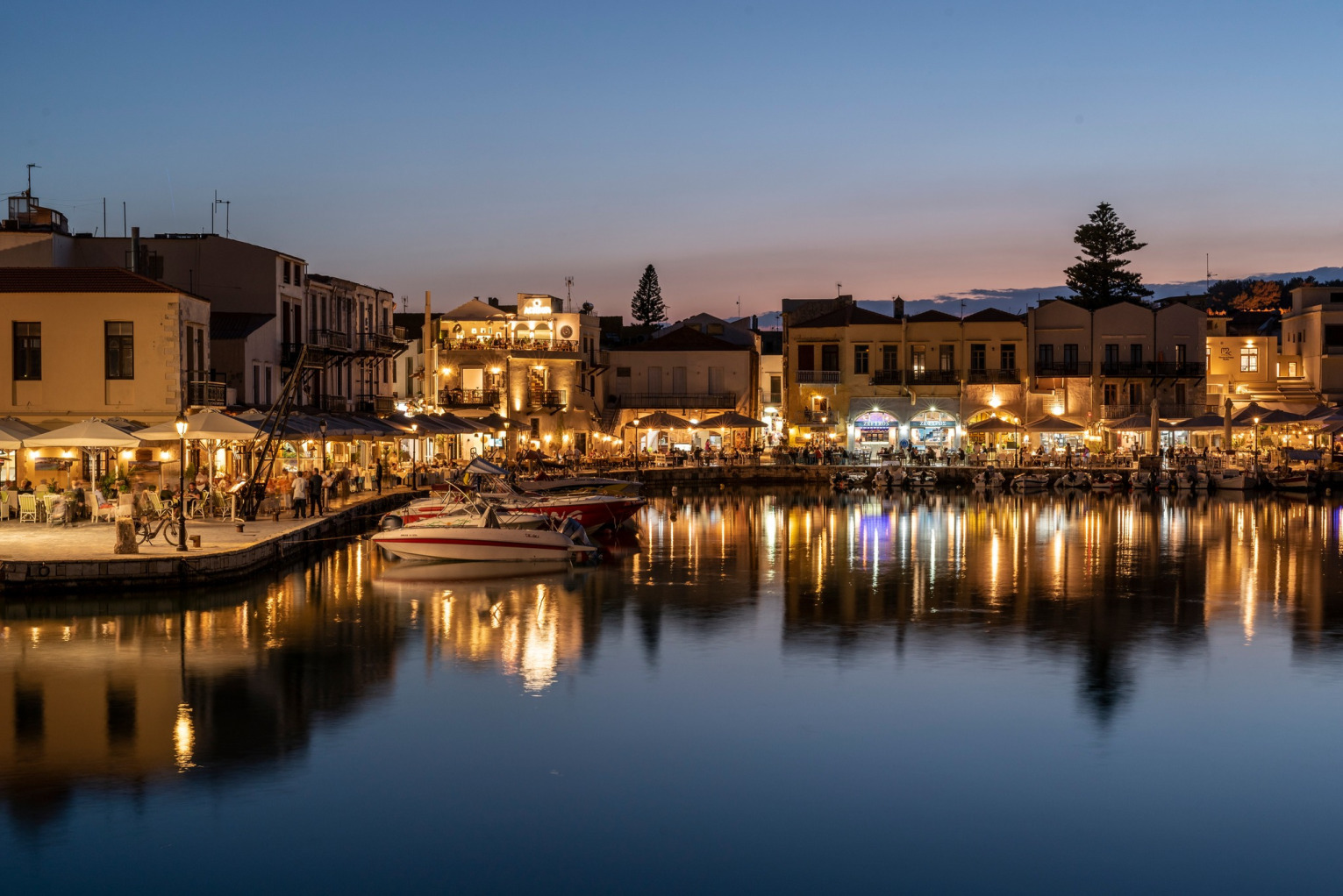 The scenic Venetian Harbor in Rethymno, Crete, featuring the Egyptian Lighthouse and historical old town buildings.