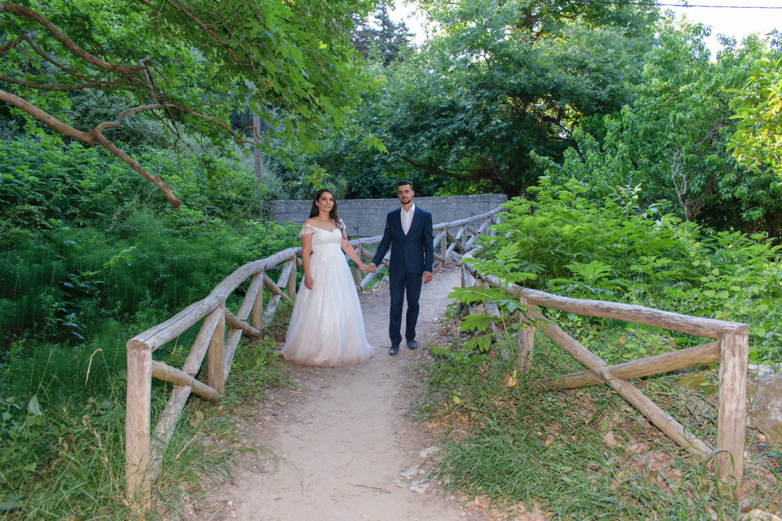 "Newlywed couple embracing on a wooden bridge inside the lush Myli Gorge, Rethymno, Crete, surrounded by waterfalls and ancient watermill ruins."